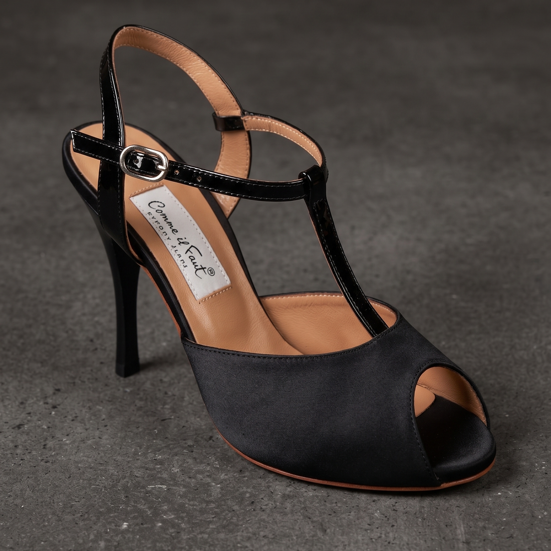 A single black satin high-heeled sandal with an open toe, T-strap, and ankle buckle strap, photographed on a dark textured gray background. 